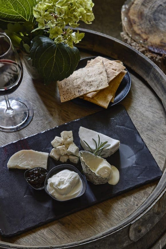 Platter of cheese and crackers on a wooden barrel with a glass of wine.